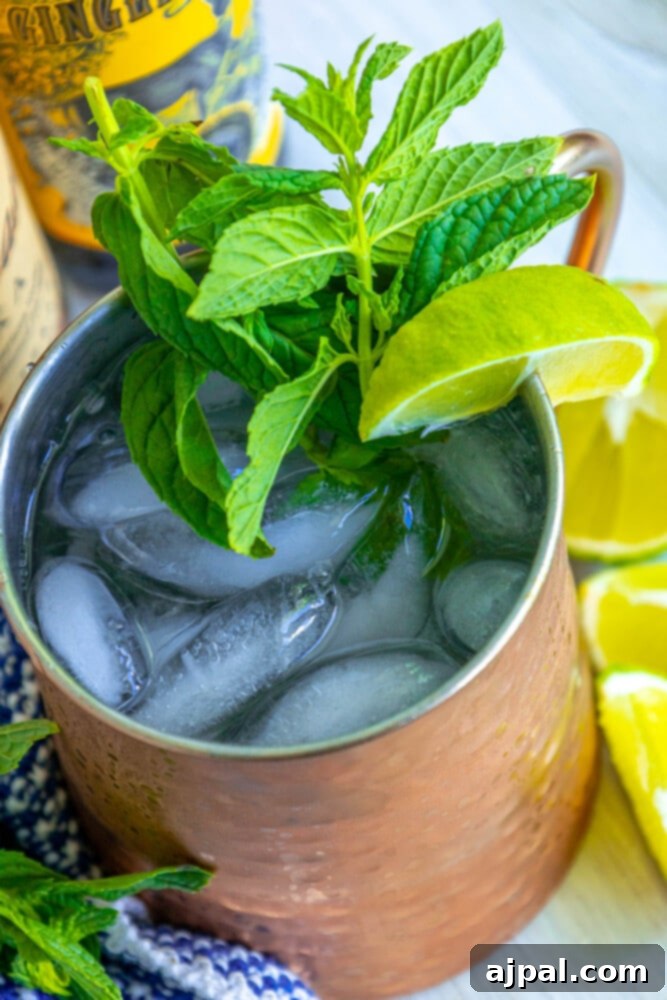 Moscow Mule Zesty Ginger Delight 3 A close-up shot of a large Moscow Mule cocktail in a chilled copper mug, adorned with fresh mint and lime slices, resting on a polished wooden surface.
