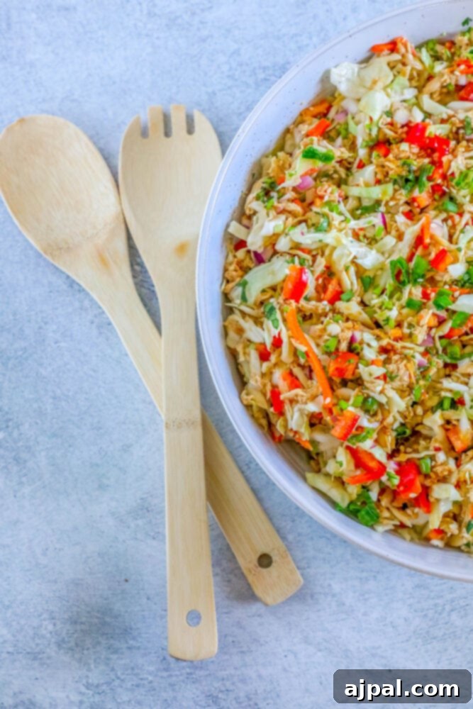 A large white bowl of Thai chicken salad with fresh ingredients on a light-colored table.