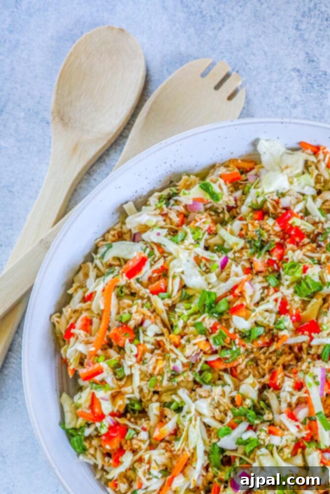Close-up of vibrant Thai chicken salad in a white bowl, showing shredded chicken, red bell peppers, green onions, and cabbage.