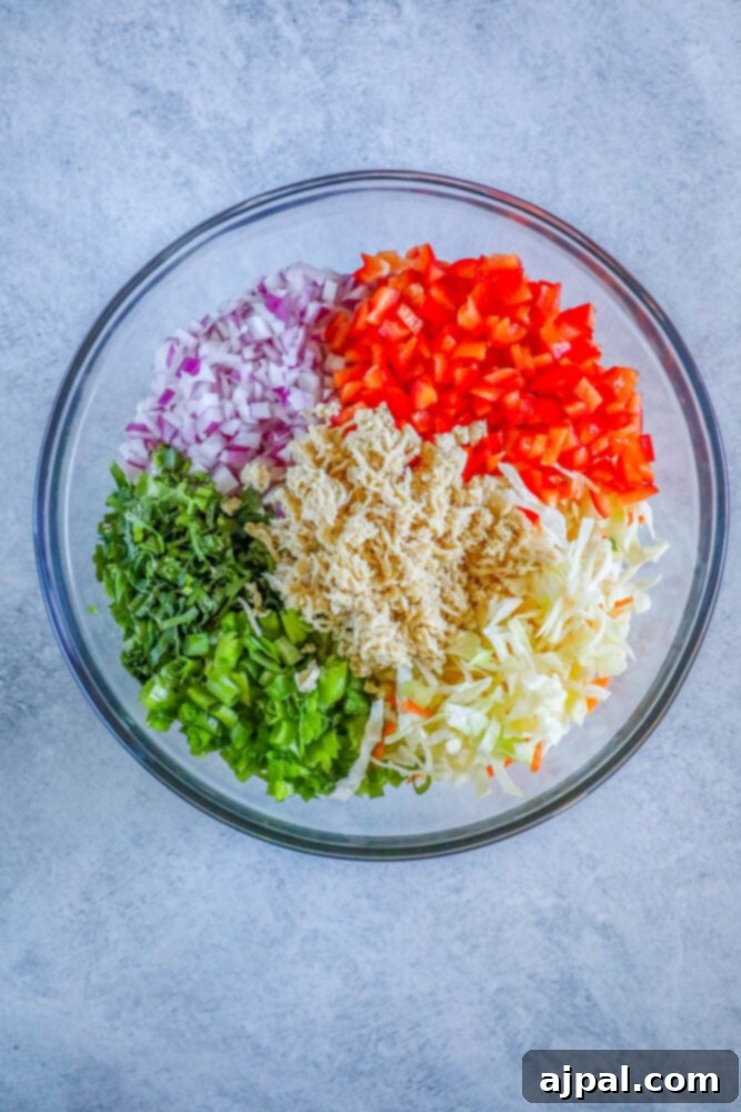 A bowl of fresh Thai chicken salad ingredients before dressing, including shredded chicken, bell peppers, and various onions.