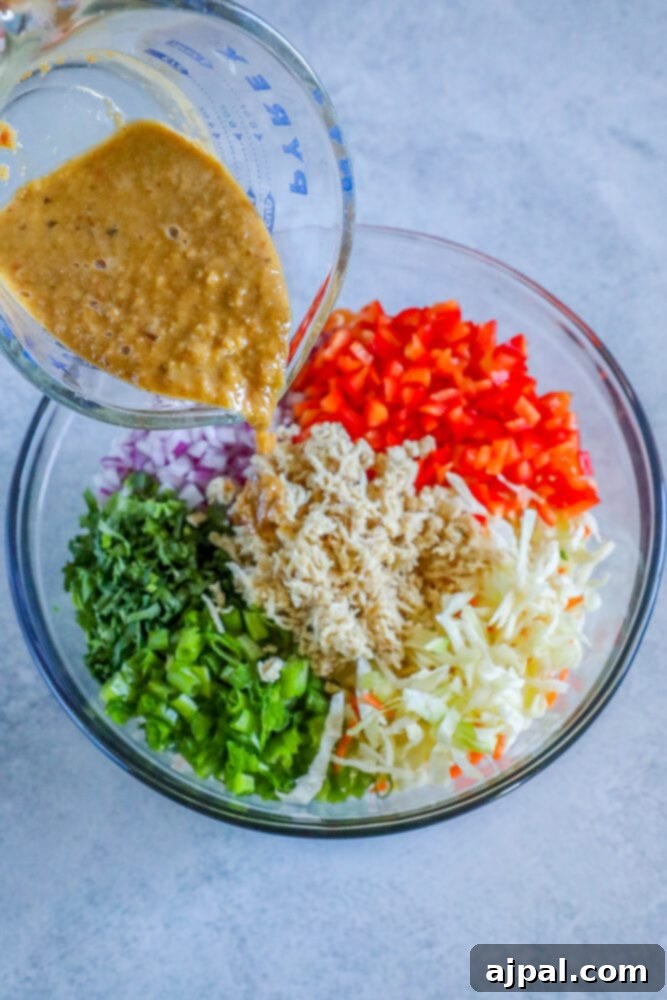 Ginger dressing being poured over a large bowl of Thai chicken salad ingredients.