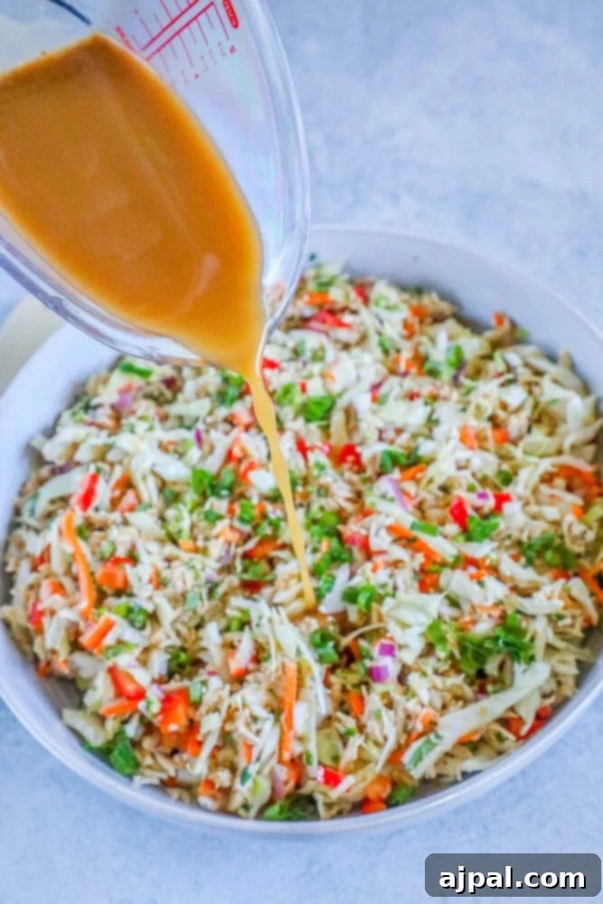 A hand drizzling ginger dressing over a fresh Thai chicken salad, highlighting the vibrant colors.