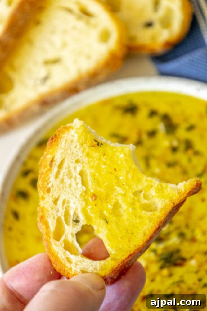 Effortless Bread Dip Perfection 2 A crisp slice of French bread poised next to a shallow bowl filled with an herb-infused olive oil bread dip, ready for dipping.