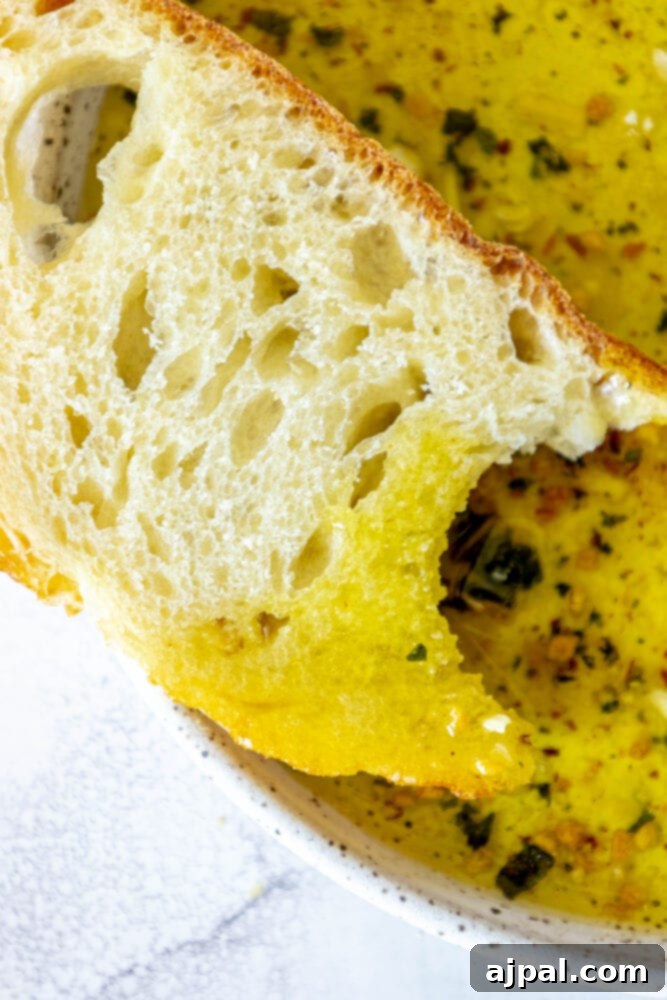 Effortless Bread Dip Perfection 4 A close-up shot of a bowl brimming with a golden olive oil bread dip, surrounded by slices of various breads and fresh herbs, highlighting its appeal as an easy, flavorful appetizer.