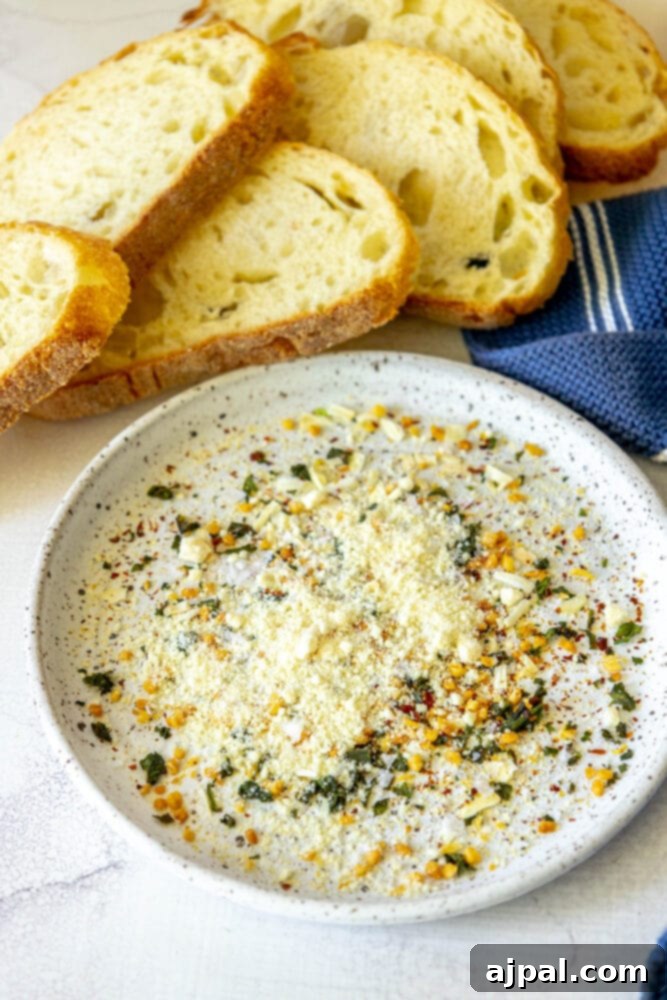 Effortless Bread Dip Perfection 5 A close-up of a bowl filled with an array of vibrant dried herbs, spices, and grated Parmesan cheese, ready to be mixed into an olive oil dip.