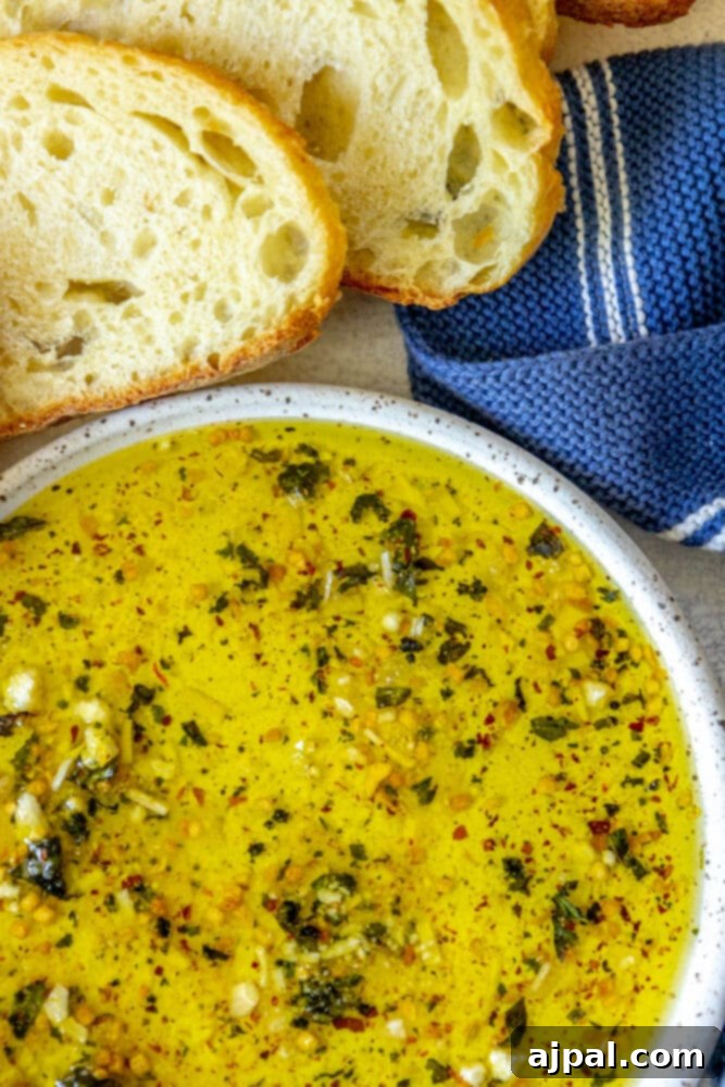 Effortless Bread Dip Perfection 8 A rustic bowl of easy olive oil bread dip, presented alongside slices of French bread and a charming blue linen napkin, creating an inviting appetizer setup.