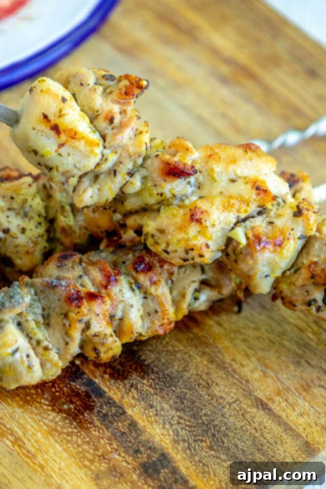 Picture of perfectly grilled chicken souvlaki on a skewer, resting on a rustic wooden cutting board