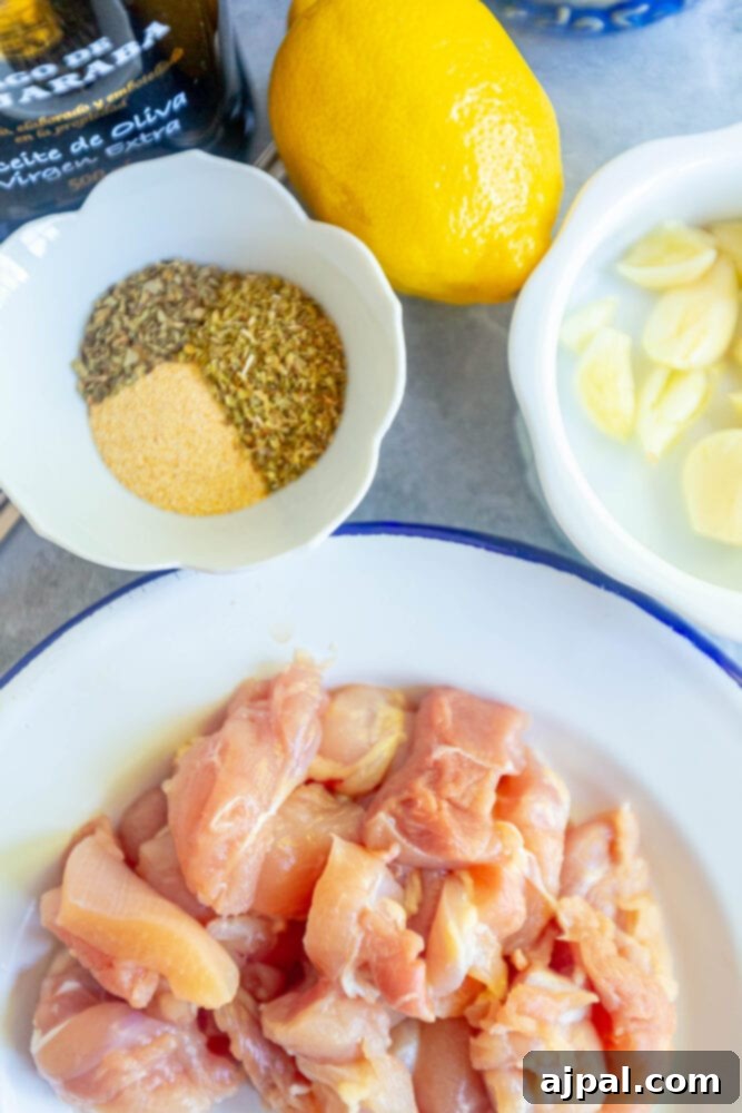 Assortment of raw chicken thighs, fresh lemon, whole garlic cloves, and dried herbs on a table, ready for marination.