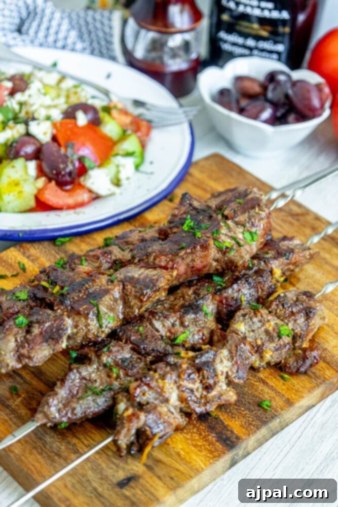 Classic Grilled Lamb Souvlaki Skewers 10 picture of lamb souvlaki on wooden cutting board with chopped cilantro on top in front of a greek salad on a plate