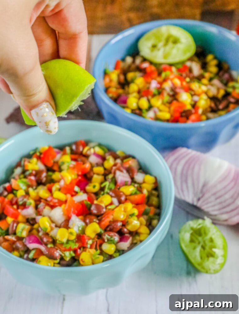 A close-up of colorful black bean and corn salsa in two blue bowls, served with tortilla chips on a wooden table.