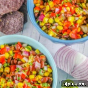 picture of salsa with beans, pepper, onion, corn, and herbs in two blue bowls on a table with chips