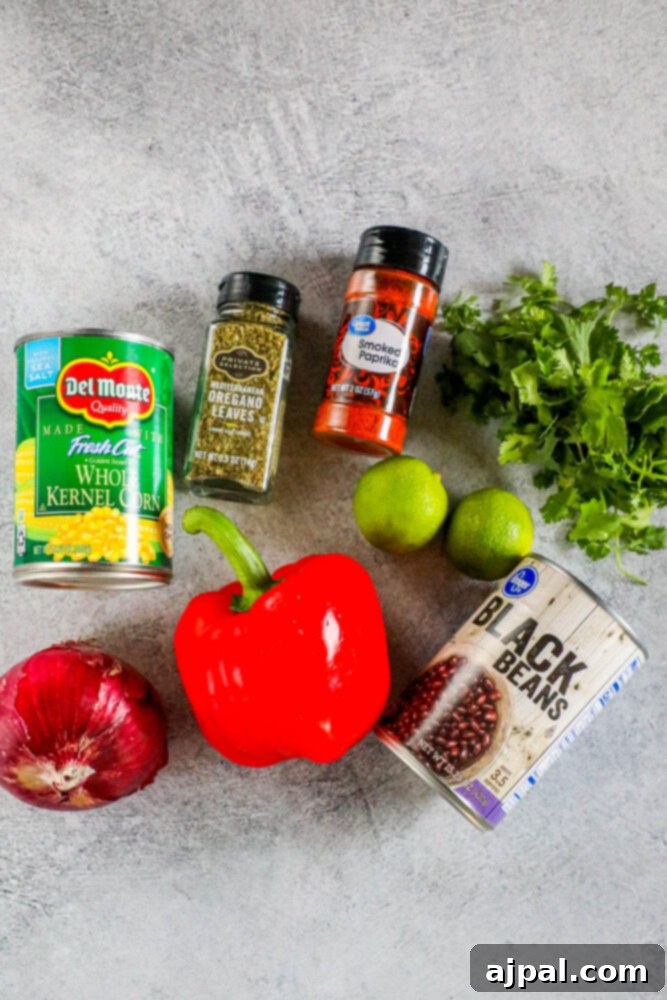 Various fresh ingredients for black bean and corn salsa laid out: beans, pepper, onion, corn, limes, cilantro, and herbs on a table.