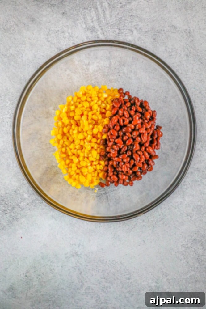 A glass bowl filled with corn and black beans, ready for salsa preparation.