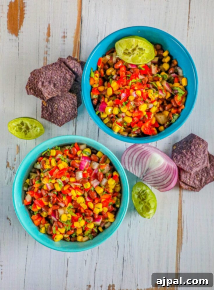 Two blue bowls filled with black bean and corn salsa, garnished with cilantro, served with tortilla chips.