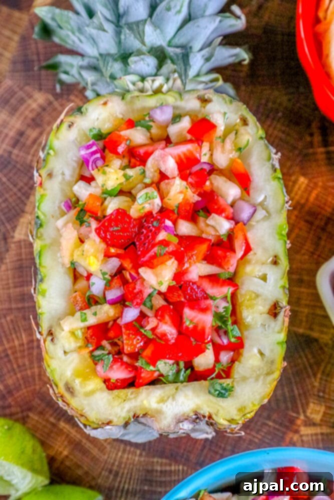 Pineapple salsa on a wooden cutting board with fresh strawberries scattered around.
