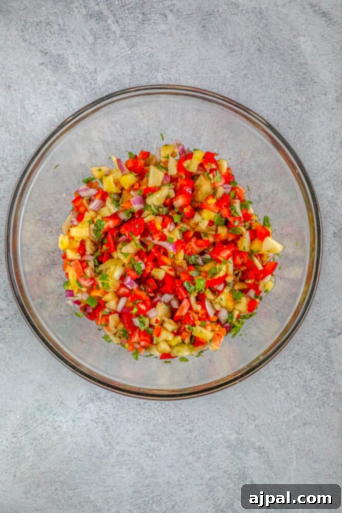 A bowl filled with freshly mixed pineapple, jalapeno, strawberries, red onion, cilantro, and red bell pepper salsa on a wooden table.