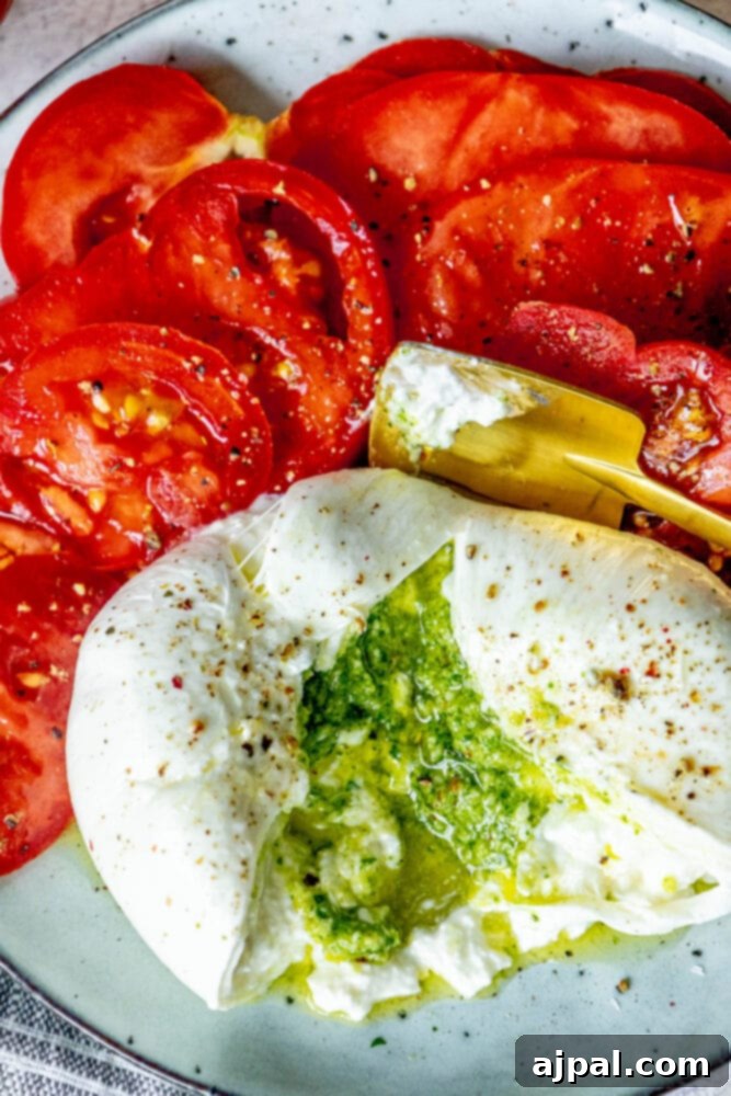 Burrata Bursting with Pesto 2 picture of burrata stuffed with pesto sliced open on a plate with sliced tomatoes