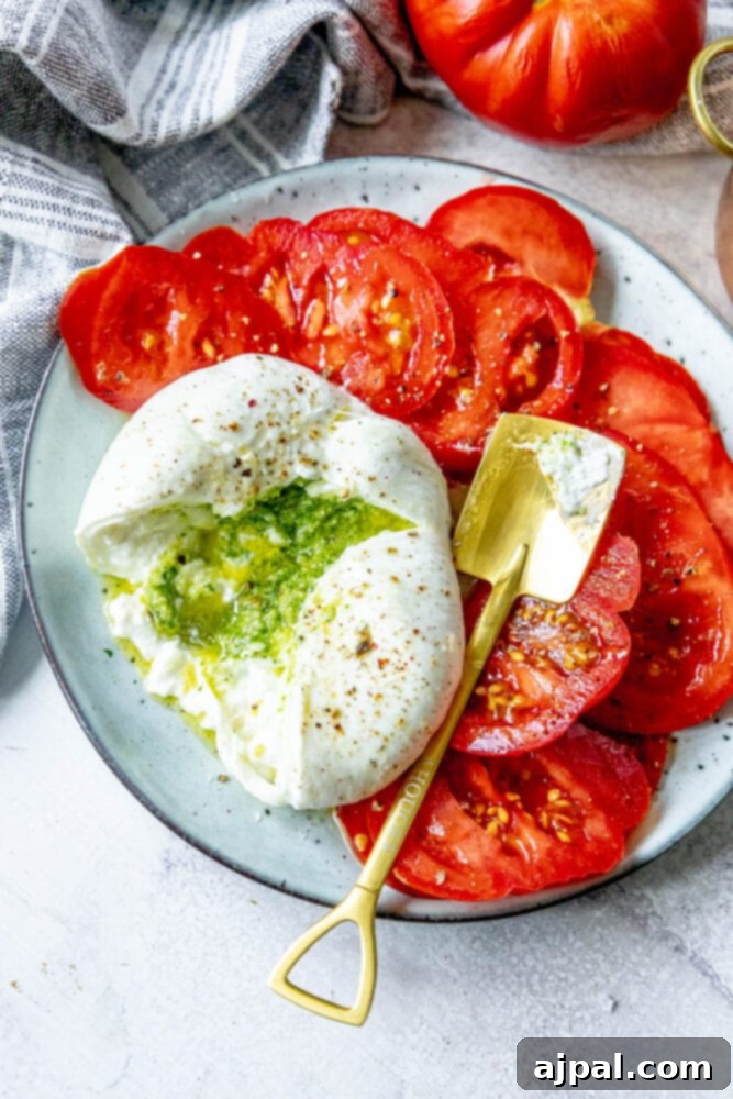 picture of burrata stuffed with pesto sliced open on a plate with sliced tomatoes