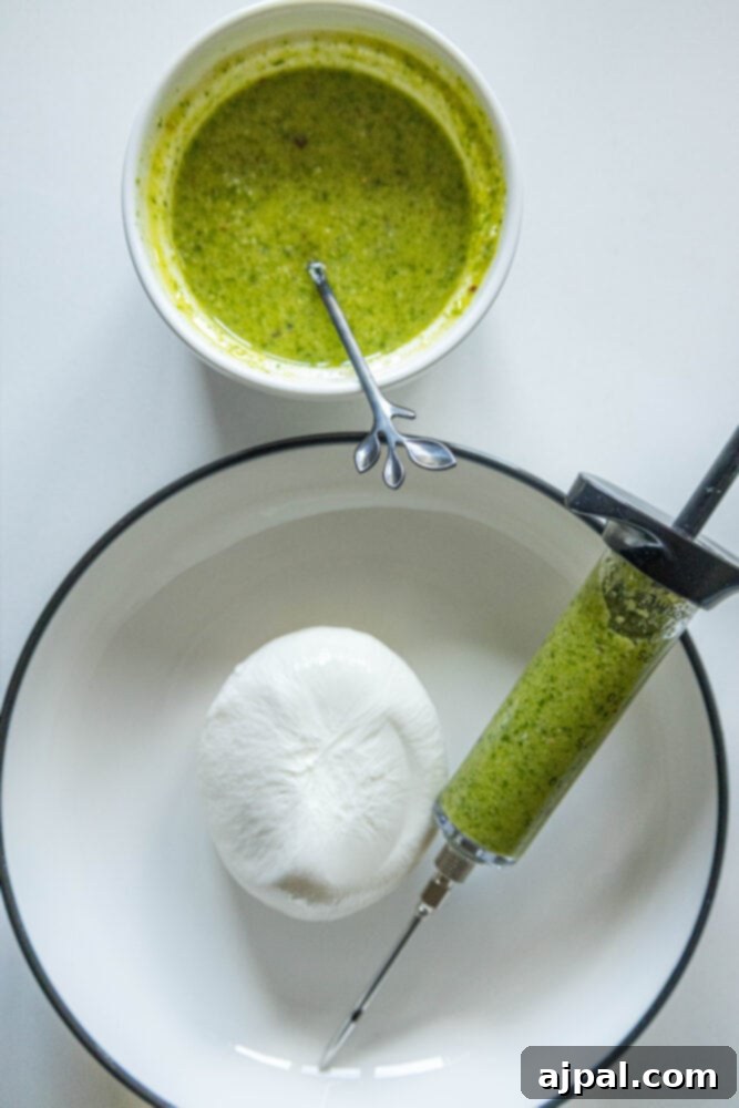 Burrata Bursting with Pesto 5 picture of a cup of pesto on a table next to a burrata in a bowl and a flavor injector syringe filled with pesto in a bowl