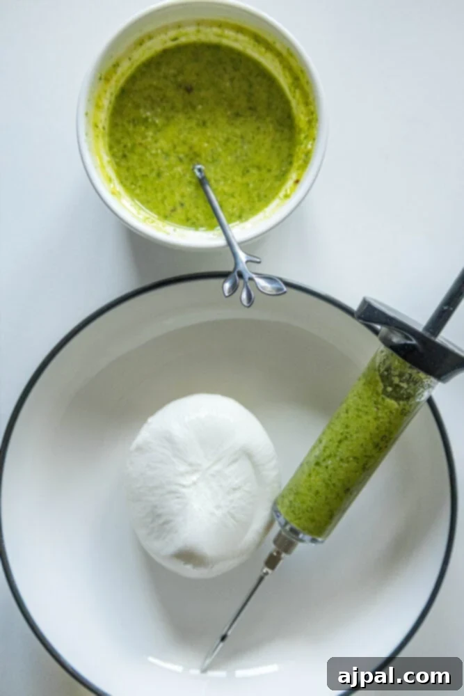 picture of a cup of pesto on a table next to a burrata in a bowl and a flavor injector syringe filled with pesto in a bowl