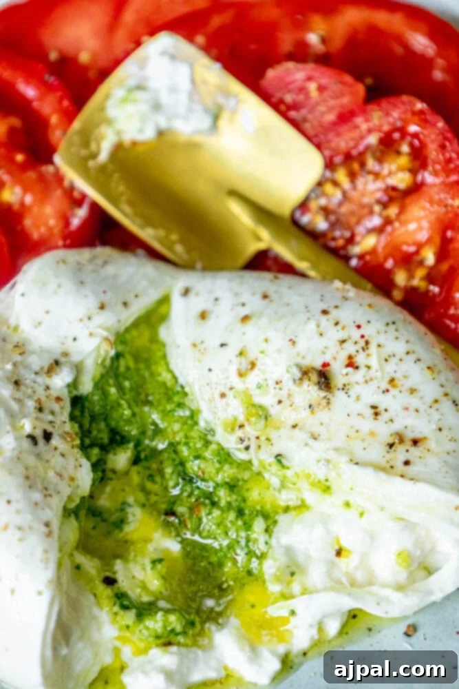 Burrata Bursting with Pesto 8 picture of burrata stuffed with pesto sliced open on a plate with sliced tomatoes