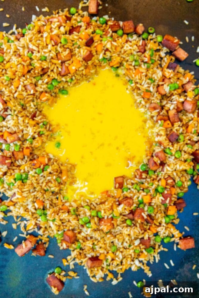Effortless Spam Fried Rice 9 picture of eggs fying in the middle of fried peas, carrots, onions, rice, and SPAM on a griddle
