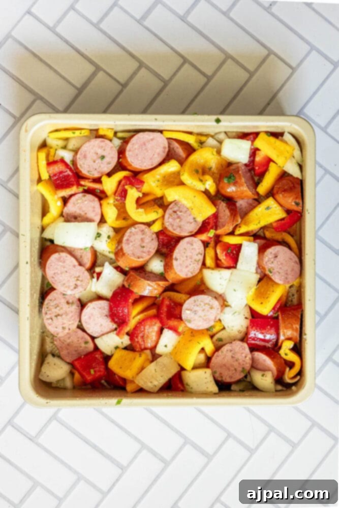 Easy Kielbasa Sheet Pan Dinner 7 picture of sliced bell peppers, onions, and turkey kielbasa tossed in herb dressing in a pan