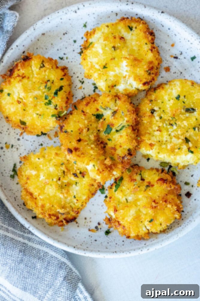 Warm Goat Cheese Bites 4 golden baked breaded goat cheese balls topped with herbs on a white speckled plate