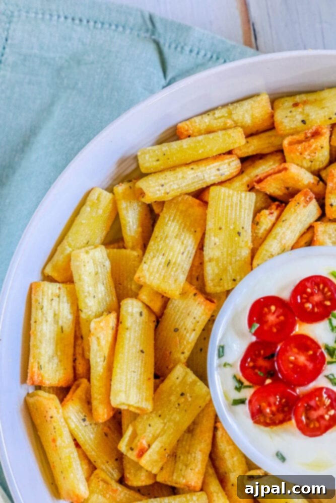 Crispy air-fried pasta chips in a bowl, served with a creamy feta dip topped with sliced tomatoes.