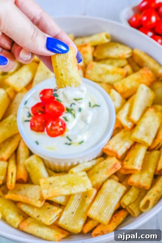 A hand dipping air-fried pasta chips into a bowl of creamy feta dip, showcasing the delightful texture and appetizing presentation.