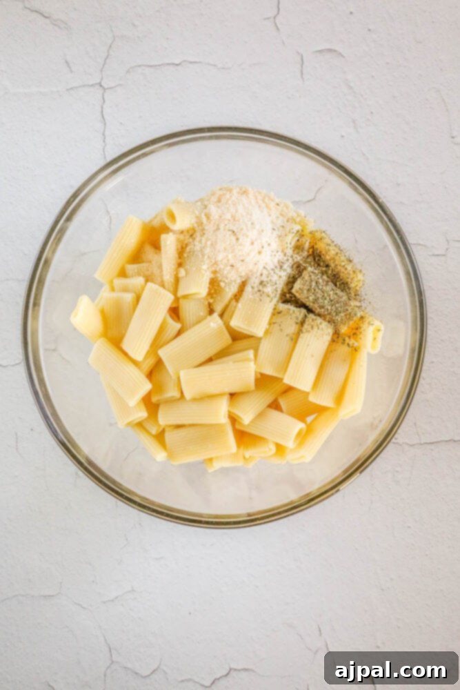 Rigatoni pasta coated with cheese and seasoning in a bowl, ready for air frying.