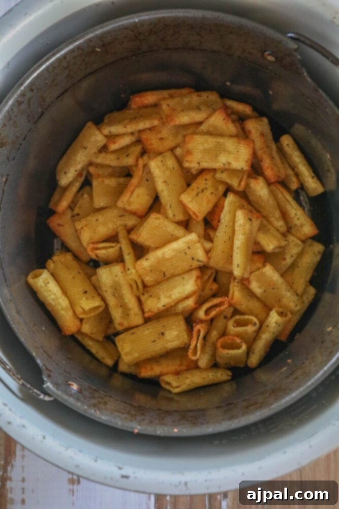 Air fryer basket filled with golden, crispy pasta chips after cooking.