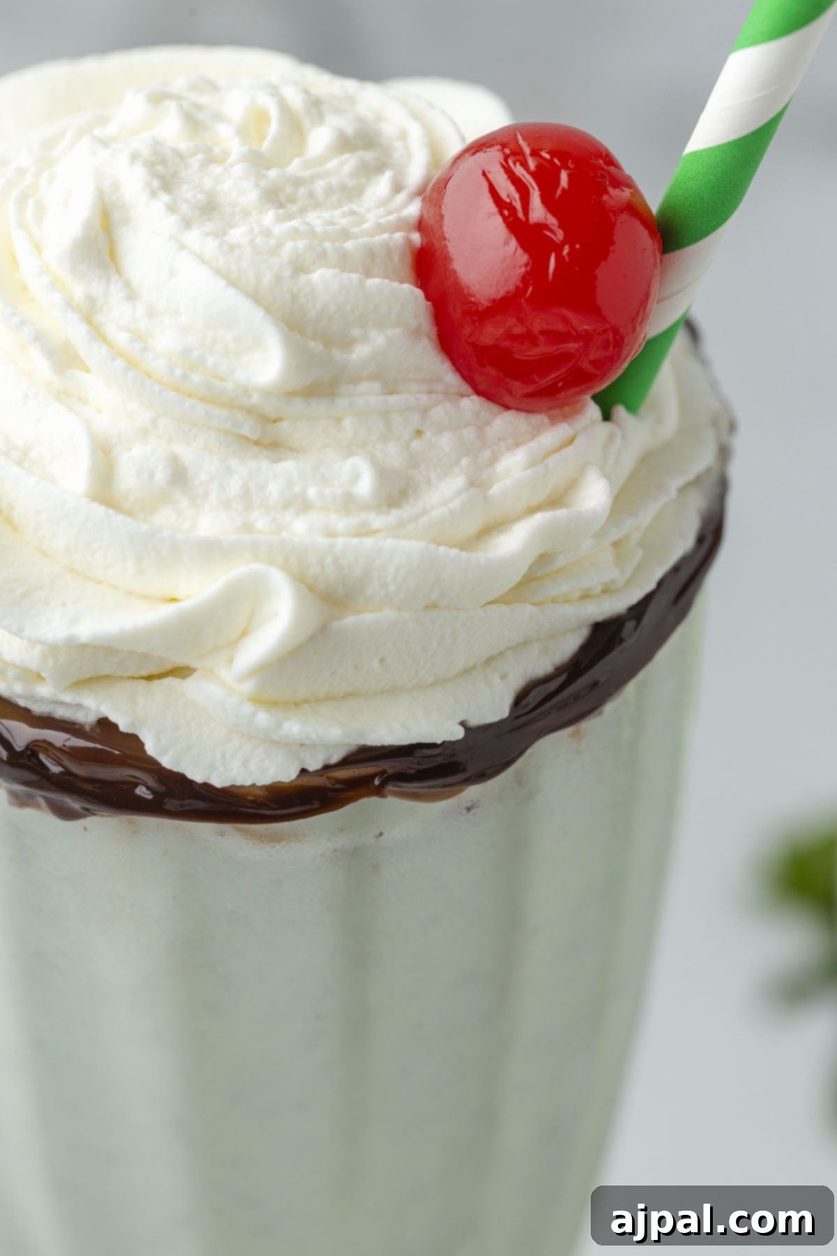 Cool Mint Swirl 2 Mint milkshake in a tall glass cup with whipped cream and a cherry on top, and a straw on the side, ready to be enjoyed.