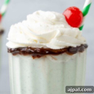 Cool Mint Swirl 12 Mint milkshake in a tall glass cup with whipped cream and a cherry on top, and a straw on the side.