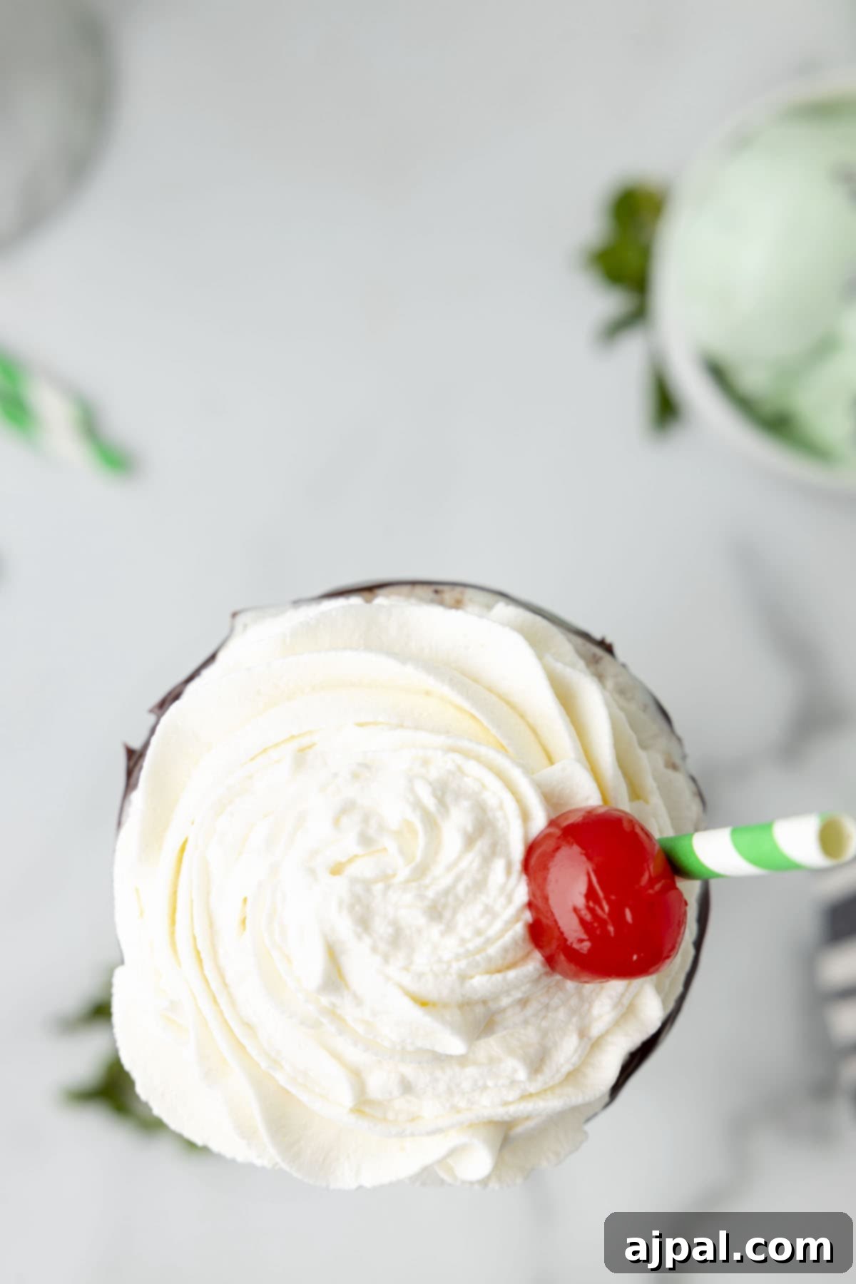 Cool Mint Swirl 8 A homemade mint milkshake served in a glass, crowned with an abundance of whipped cream and a single red cherry in the center.