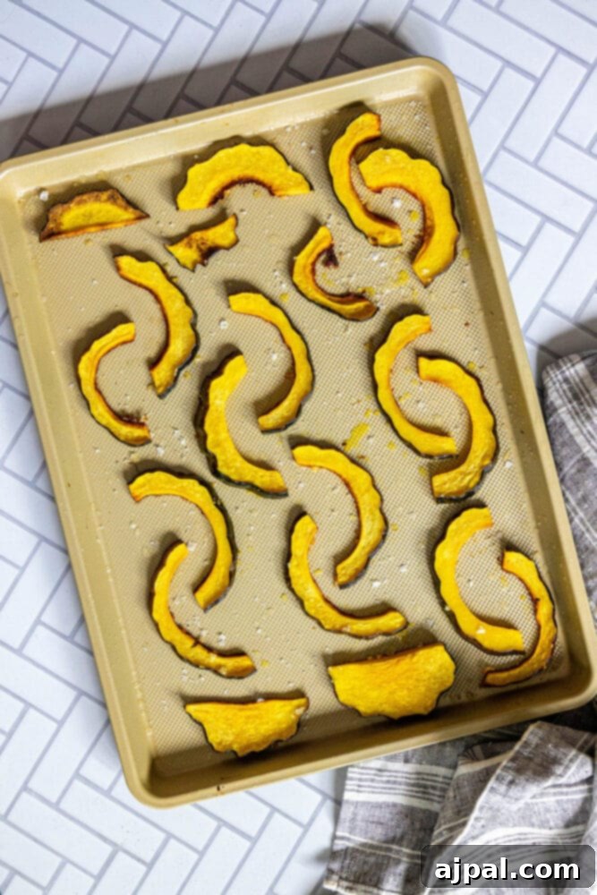 Thinly sliced acorn squash, seasoned and ready for roasting, spread on a baking sheet.