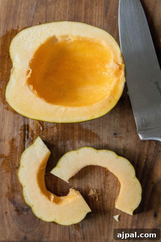 An acorn squash expertly cut in half, with one half further sliced into thin, crescent-shaped strips on a cutting board beside a sharp knife.
