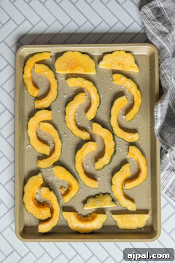 Thinly sliced acorn squash rings, glistening with olive oil and seasoned with salt, meticulously arranged on a parchment-lined baking sheet, ready for roasting.