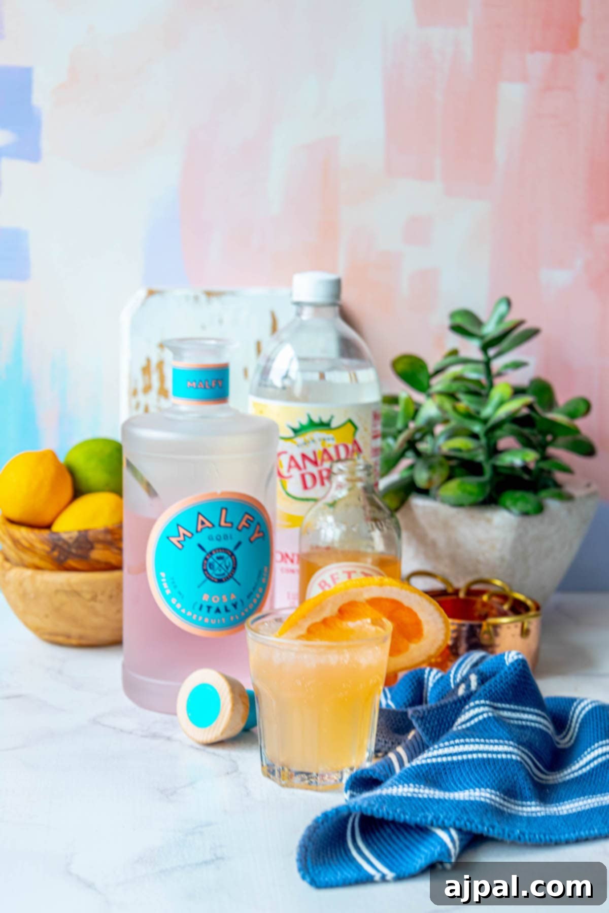 Glass with grapefruit gin fizz, gin, and grapefruit soda on a table