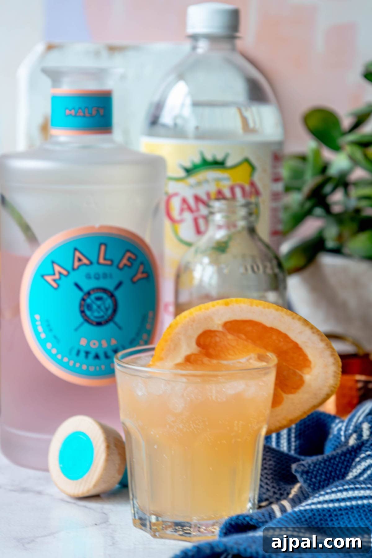 Glass with grapefruit gin fizz, surrounded by gin bottle and grapefruit soda