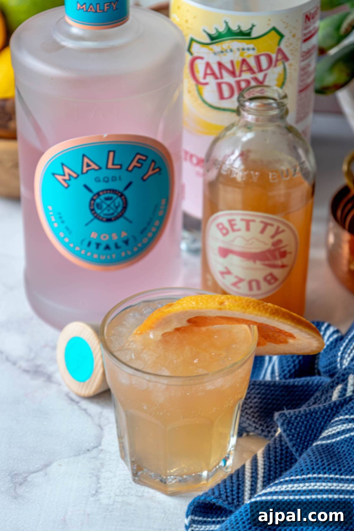 Glass with grapefruit gin fizz, gin bottle, and grapefruit soda in background