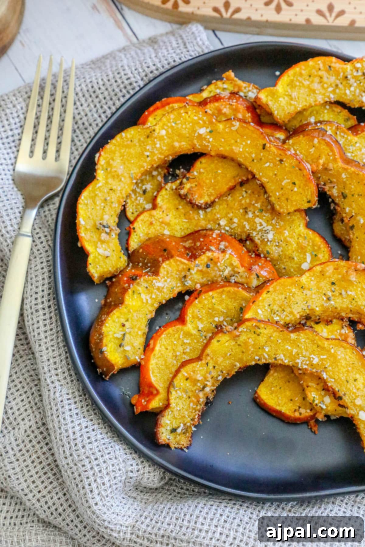 Picture of perfectly roasted acorn squash slices seasoned with herbs and spices, elegantly arranged on a black plate.
