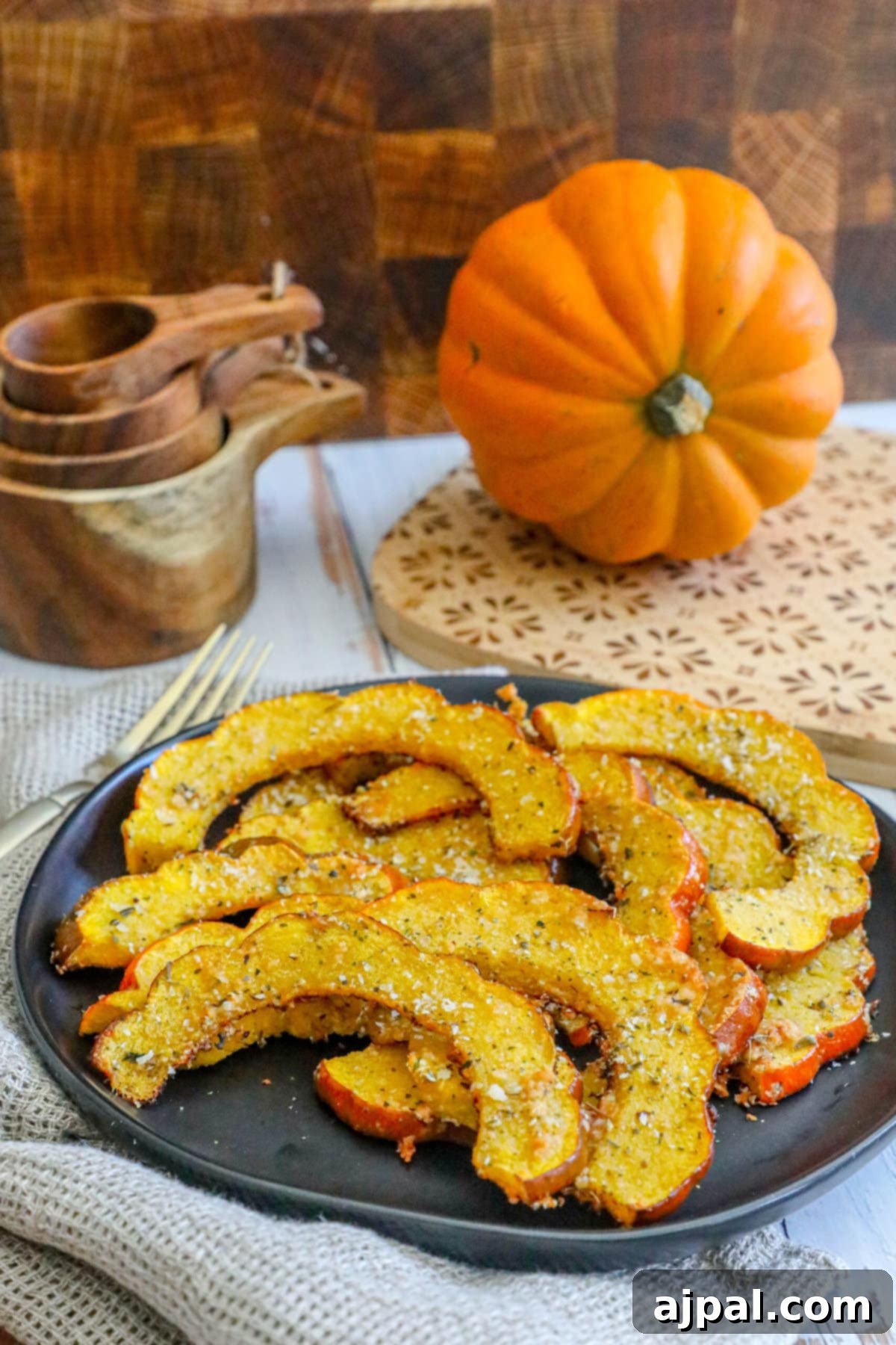 Picture of roasted acorn squash slices seasoned with herbs and spices on a black plate, ready to be served with a knife and fork.