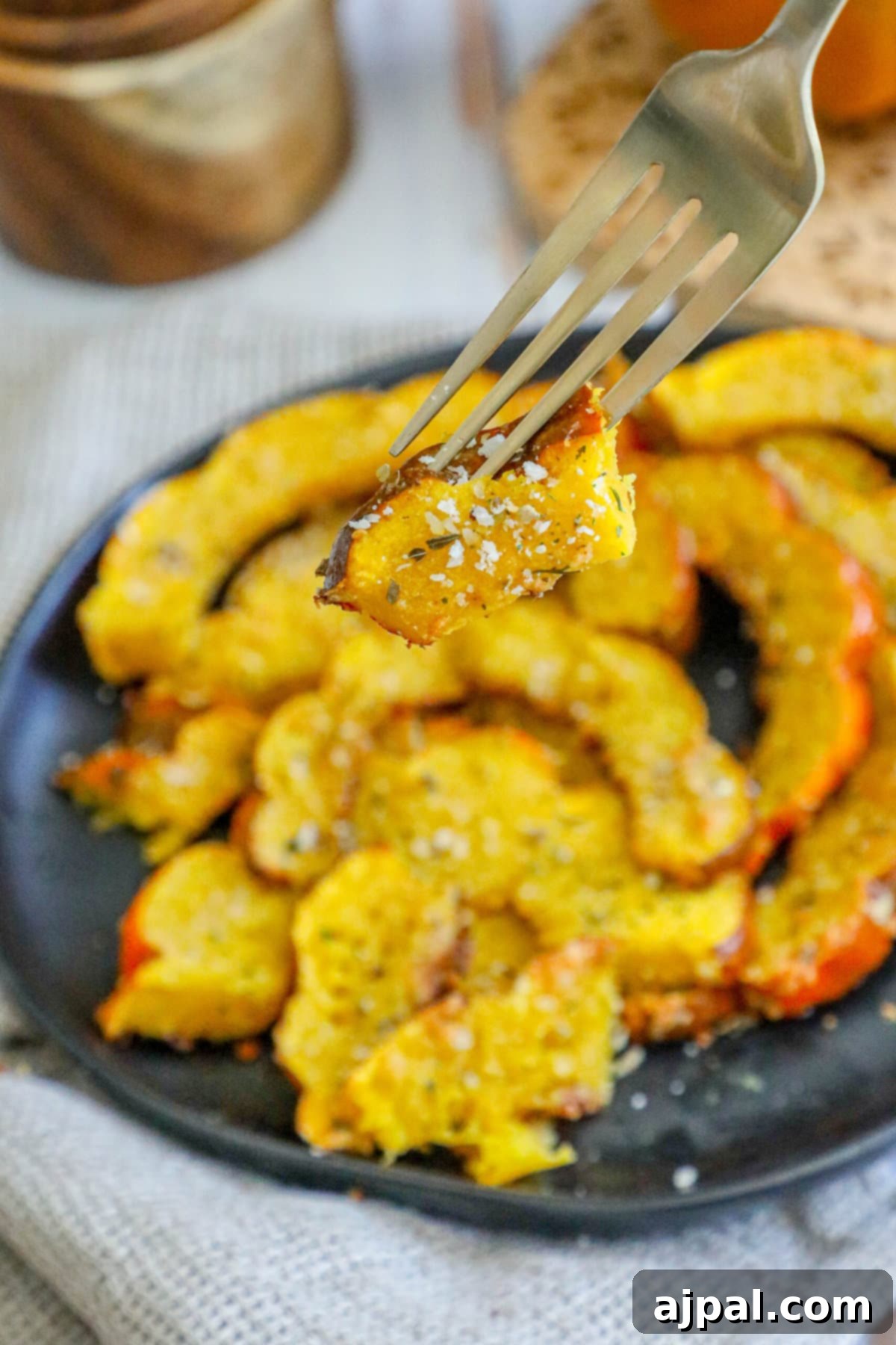 Picture of a fork being used to eat a piece of herb roasted acorn squash from a black plate.