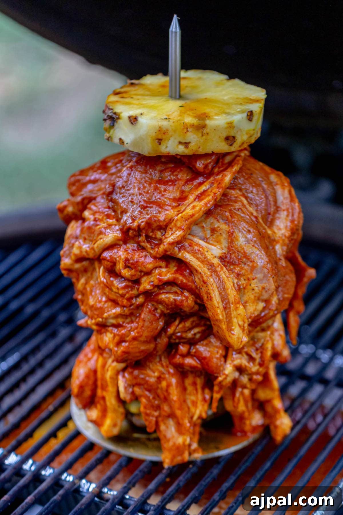 picture of raw marinated pork n a spit on a grill with a pineapple on top