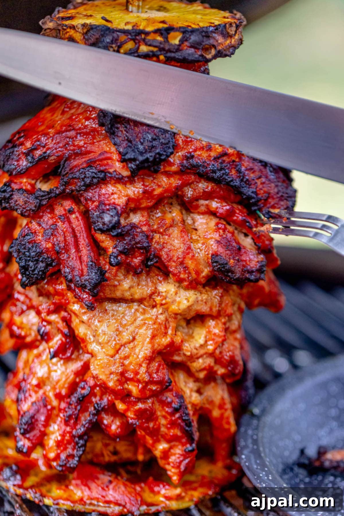 picture of a knife slicing smoked al pastor pork on a grill