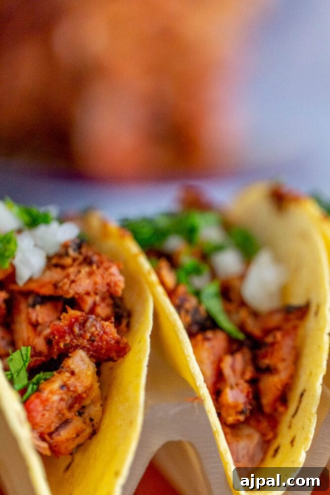 Three Easy Smoked Al Pastor tacos are sitting on top of a plate.