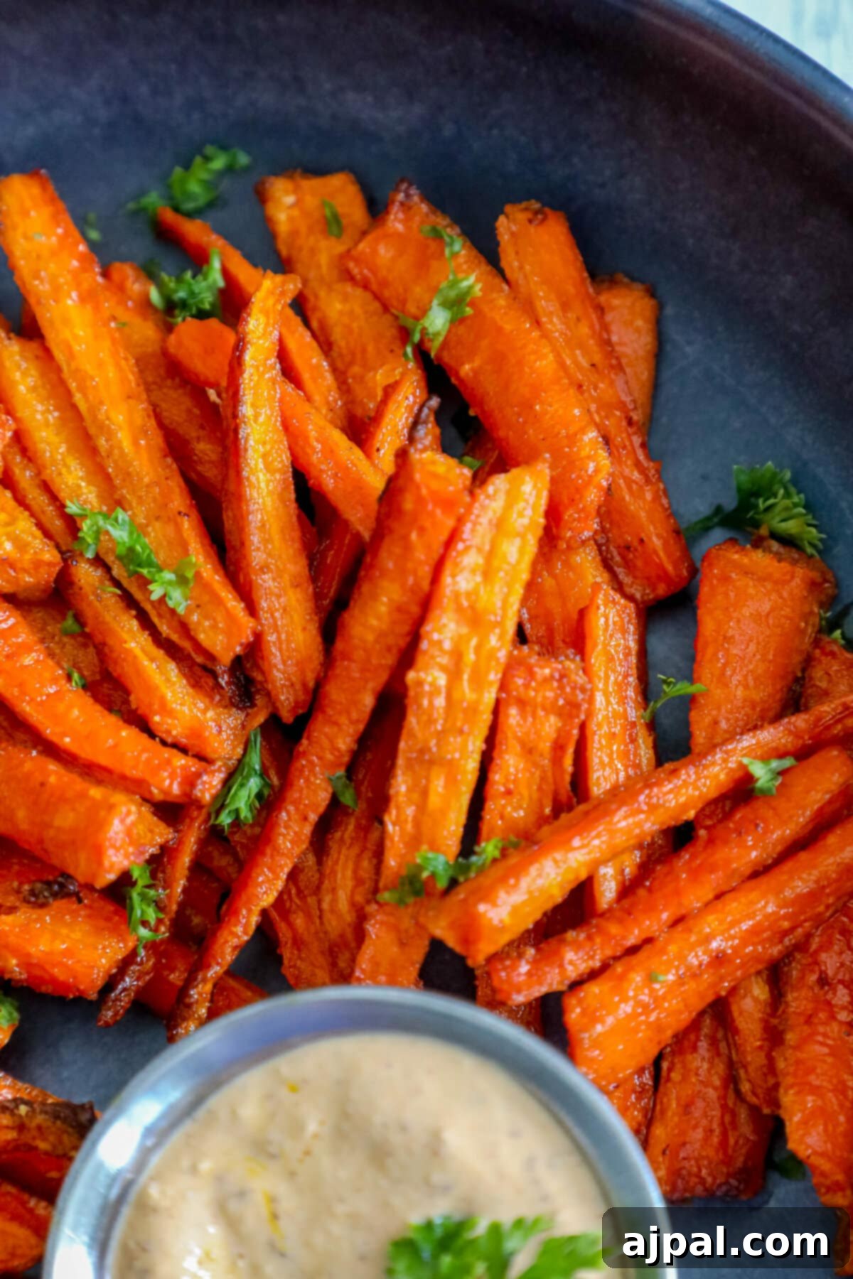 Easy carrot fries served with a dipping sauce on a plate, garnished with fresh herbs.