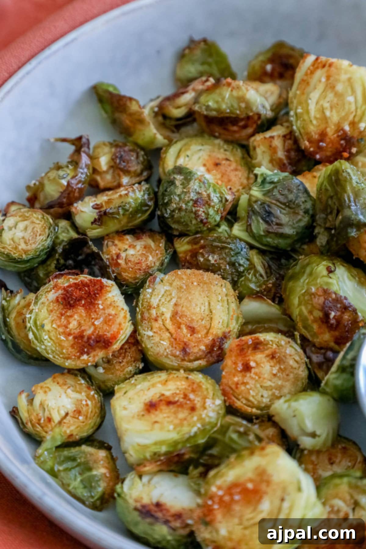 Crispy Garlic Roasted Brussels 2 Close-up picture of crispy garlic roasted Brussels sprouts in a white bowl, with a small cup of dipping sauce nearby, highlighting their golden-brown edges and delicious texture.