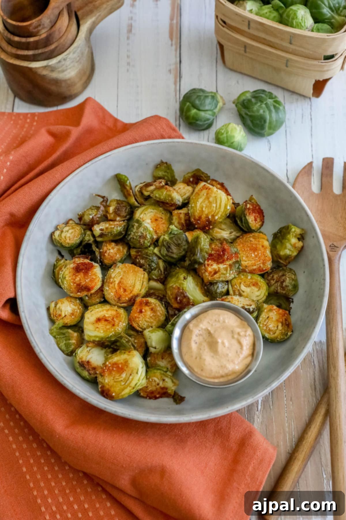 Crispy Garlic Roasted Brussels 4 A close-up of beautifully roasted garlic Brussels sprouts served on a rustic plate, perfectly golden and tender, accompanied by a small bowl of dipping sauce.